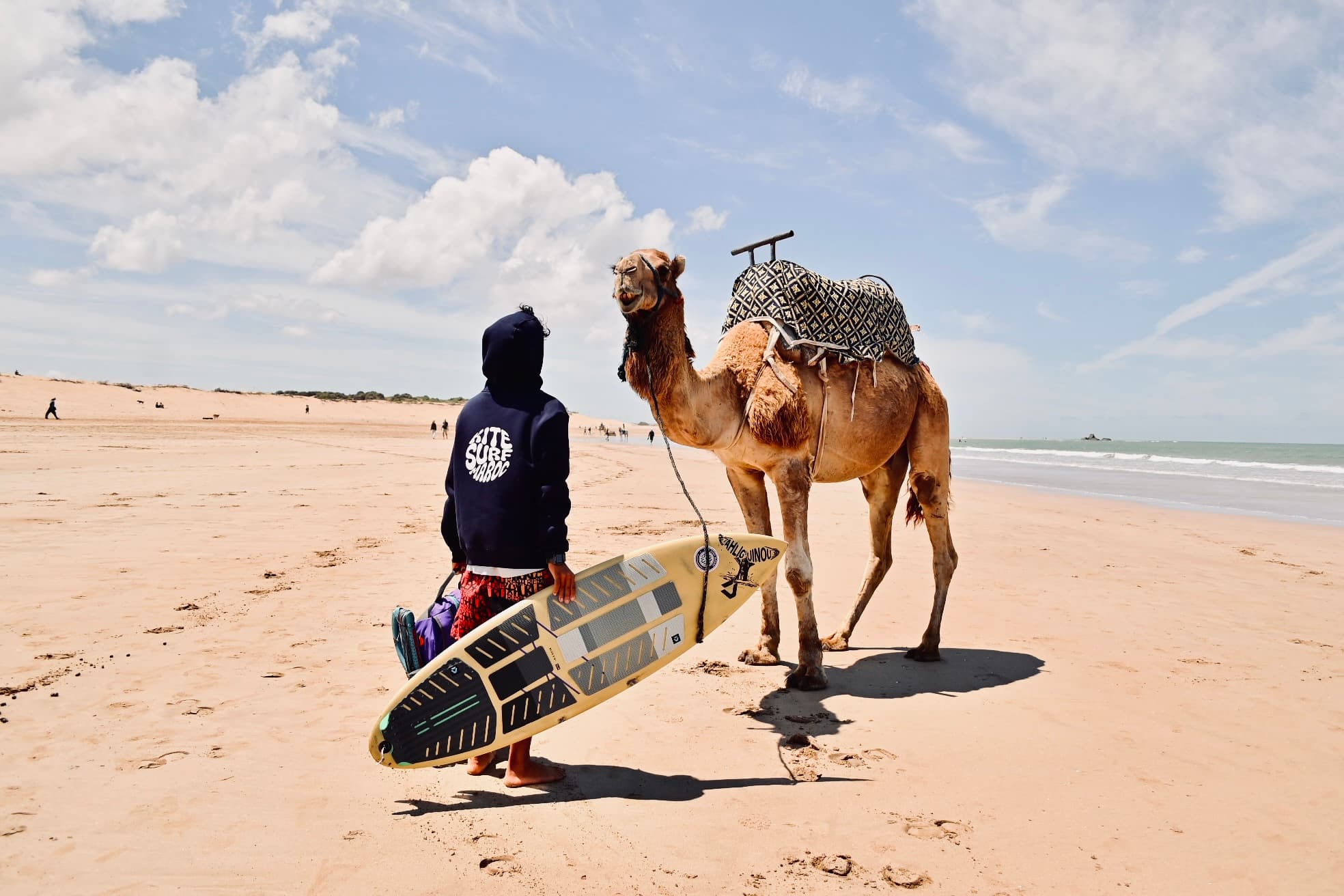 Kitesurfer with his board next to a camel on Essaouira beach
