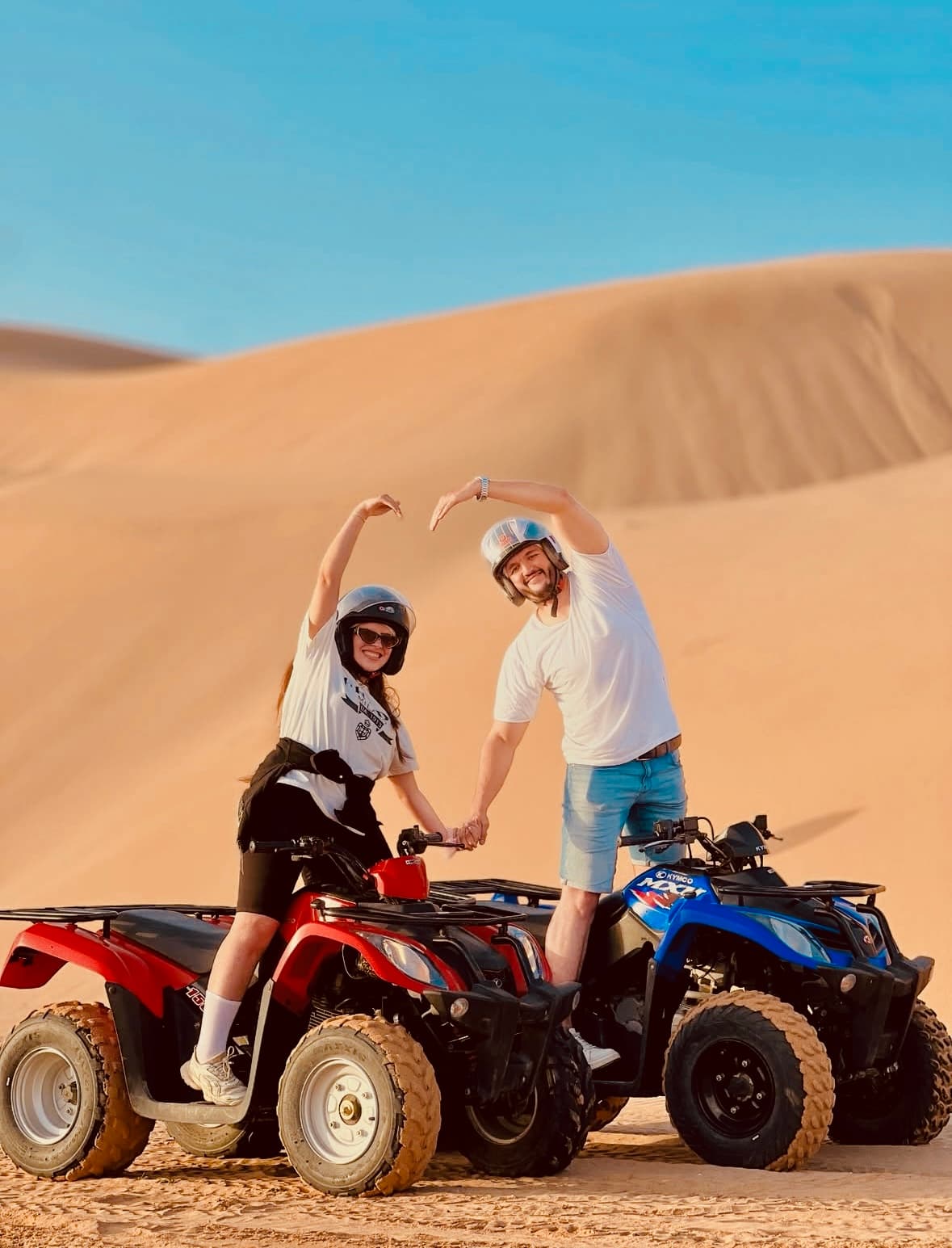 Couple making a heart on quads in the dunes
