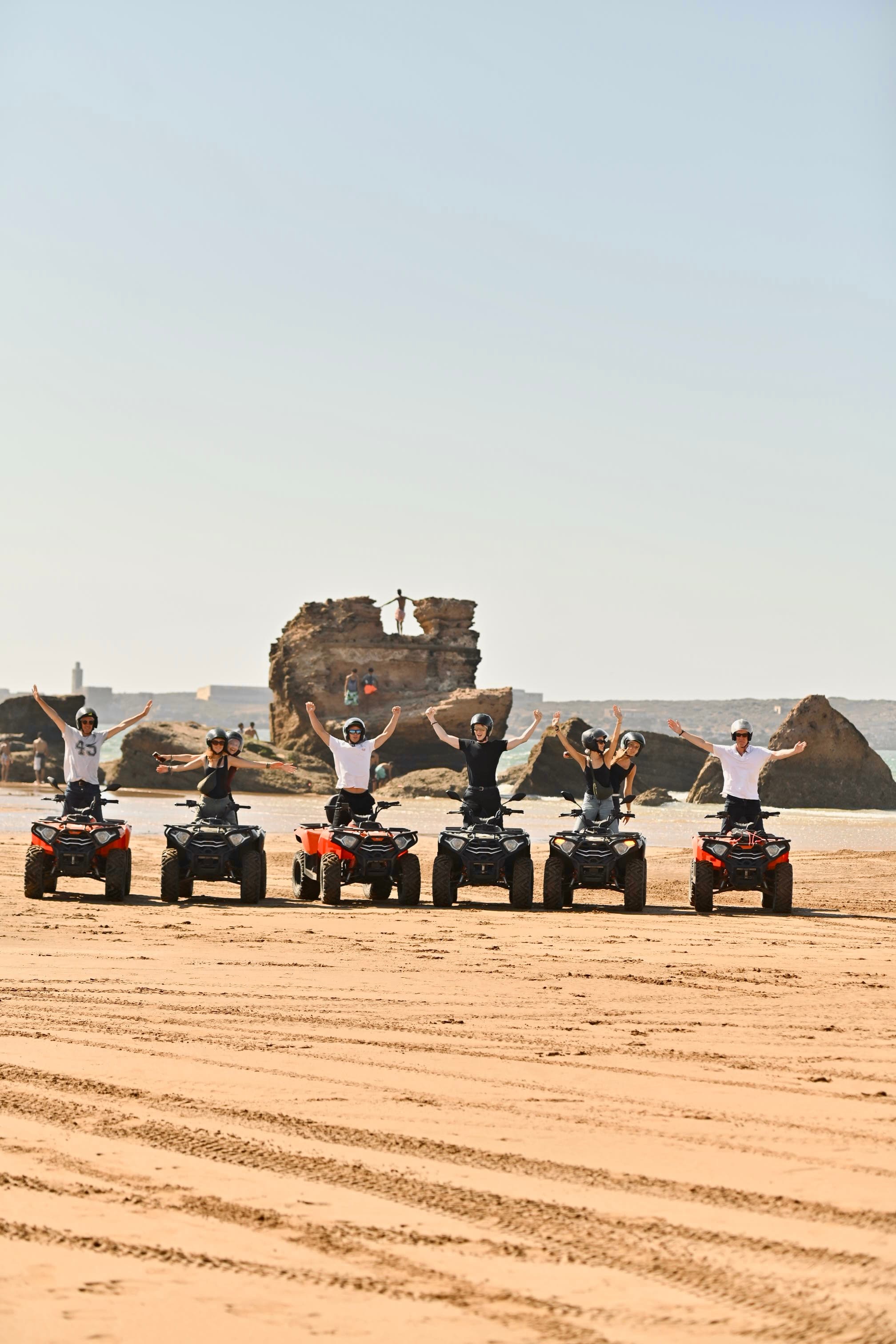 Group celebrating on quads on the beach with a rock formation behind