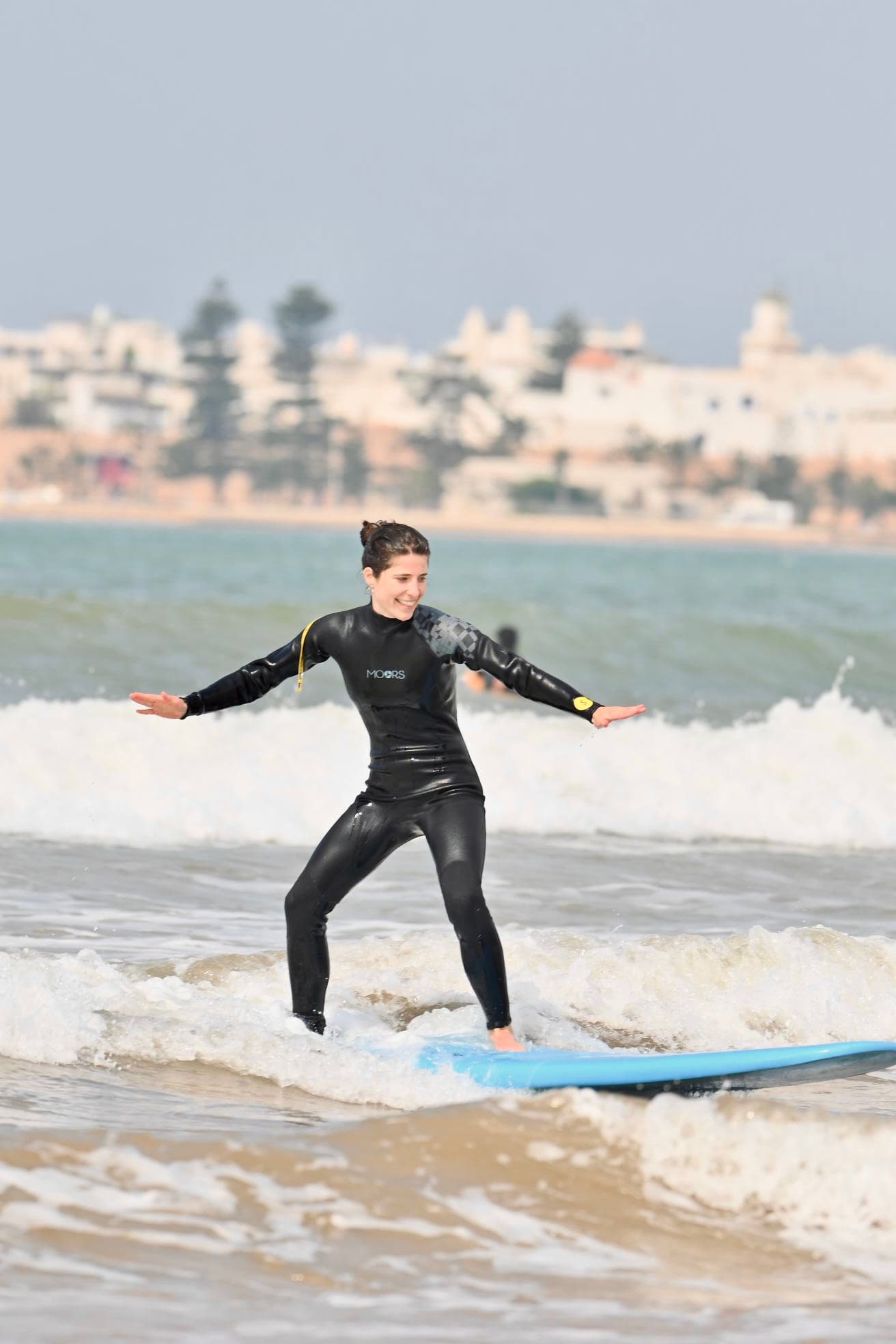 Smiling surfer riding a wave with the Essaouira medina behind